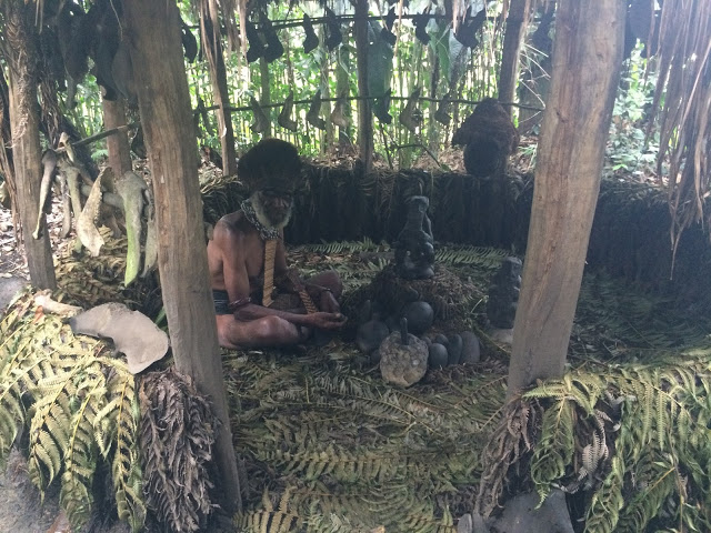 The local witchdoctor sits around a small fire in Tokua village, Mount Hagen